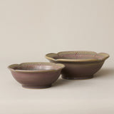 Two ceramic bowls with scalloped flower-like rims, featuring a glossy brown and muted pink glaze with fine green linear detailing inside, set against a plain beige background.