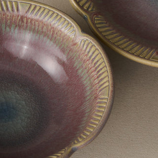 Close-up of a ceramic bowl with a scalloped rim, featuring a textured glaze in dusty mauve, olive green, and blue-gray tones, with a second matching bowl partially visible in the background.