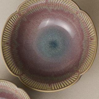 An overhead close-up of a ceramic bowl with a scalloped rim, featuring a textured glaze that transitions from a dusty rose-pink at the edges to a blue-gray center.