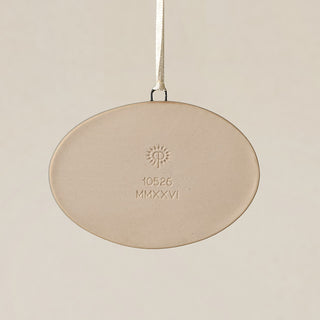 Backside of the Rookwood Findlay Market ornament in Sencha glaze: oval light beige ceramic with an embossed RP logo, item number, and 'MMXXVI' in the center, suspended by a white ribbon against a textured beige background.