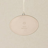 Backside of the Rookwood Queen City ornament: oval light beige ceramic with an embossed "RP logo and the text '10611. MMXXVI' in the center, suspended by a white ribbon against a textured beige background.