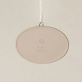 Backside of the Rookwood Union Terminal ornament in Sencha glaze: oval light beige ceramic with an embossed RP logo, item number, and 'MMXXVI' in the center, suspended by a white ribbon against a textured beige background.