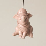 A pink ceramic pig ornament, wearing a crown and a sash that reads 'Cincinnati,' hanging from a brown ribbon against a plain light beige background.